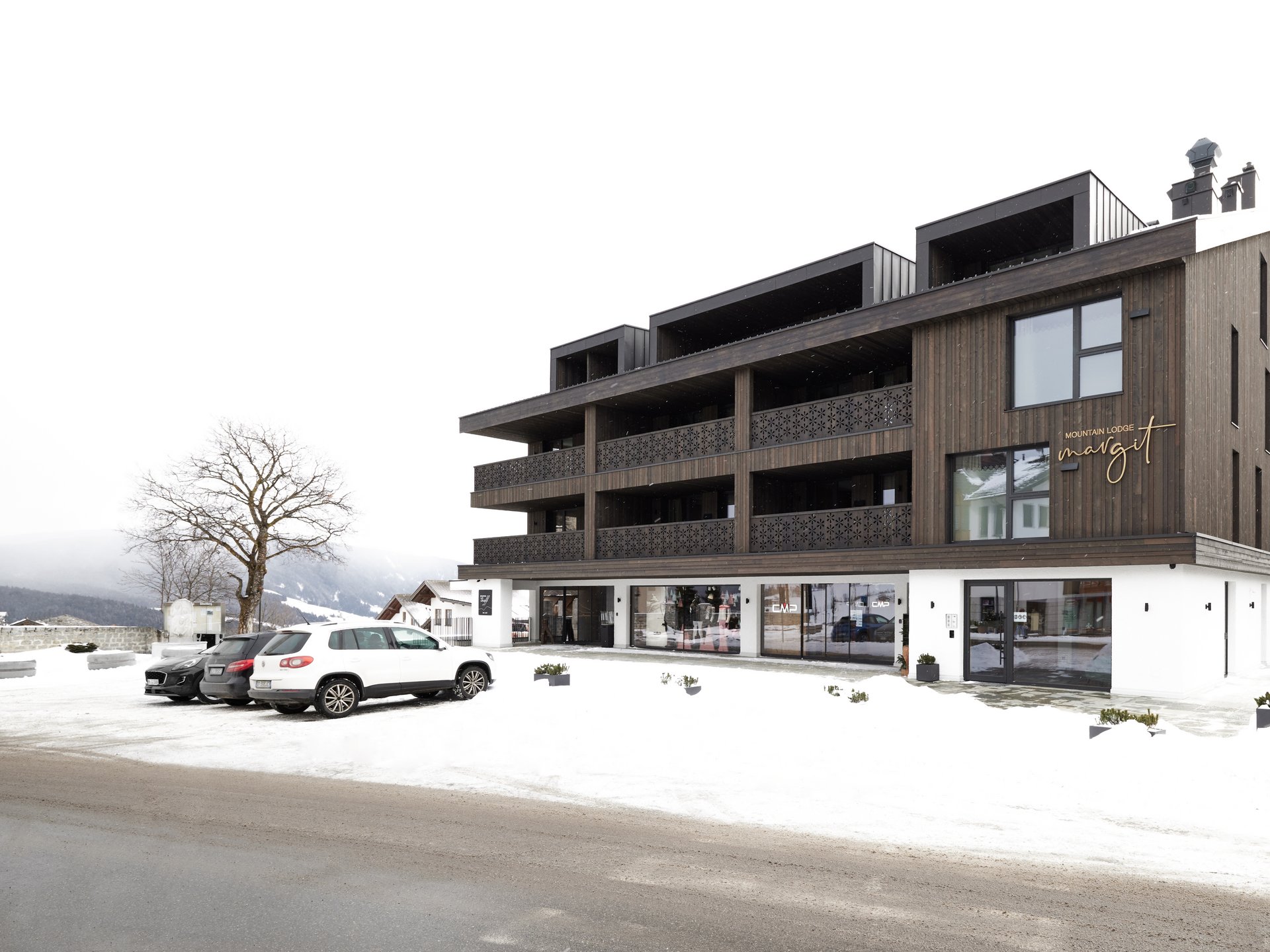 Urlaub in Südtirol: Auf in die Mountain Lodge Margit! ❋ Modernes Berglodge-Gebäude mit Parkplätzen und Schnee im Winter